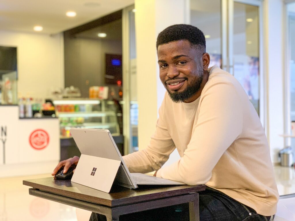 Homem negro sentado no ambiente de trabalho, com um laptop à mesa